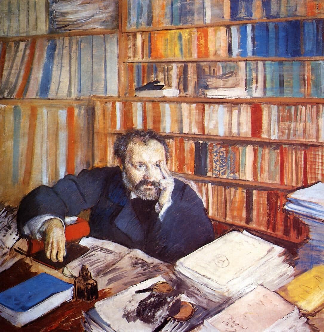 Escritor de barba, com a mão na têmpora, pensa diante de uma mesa coberta de papéis e livros.