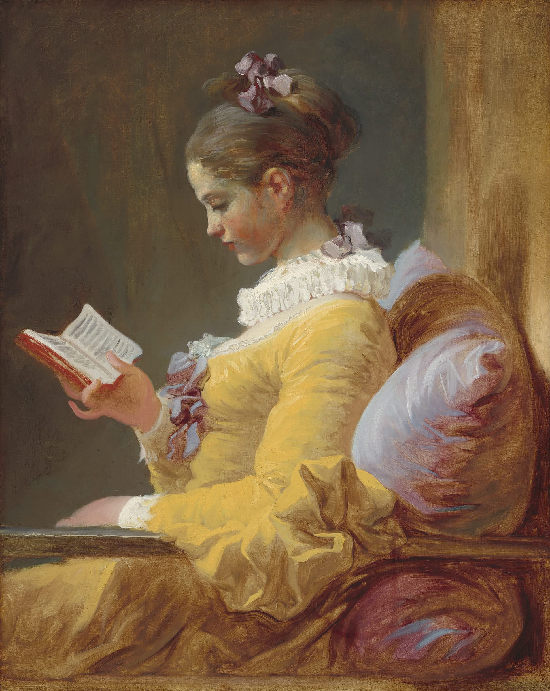 Jovem de vestido amarelo lê um pequeno livro, absorta, apoiada numa almofada.